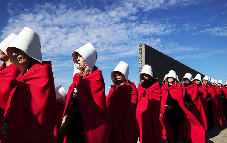 En el Parque de la Memoria, 32 mujeres vestidas con cofia blanca y vestido rojo, caminaron frente a los muros con los nombres de miles de víctimas de la dictadura